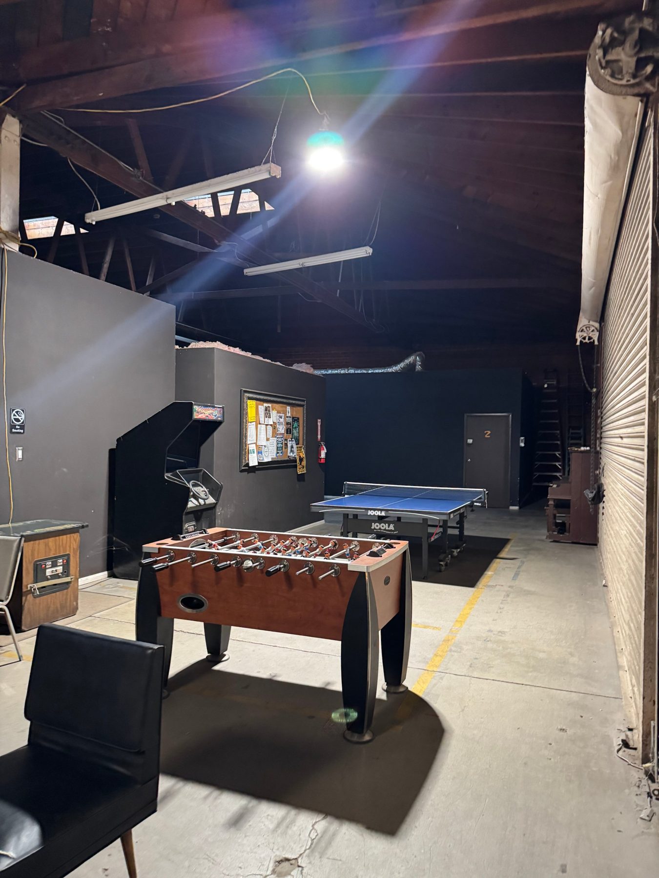 Game area with foosball, ping pong, a stand-up arcade cabinet and the community board under the wooden truss ceiling