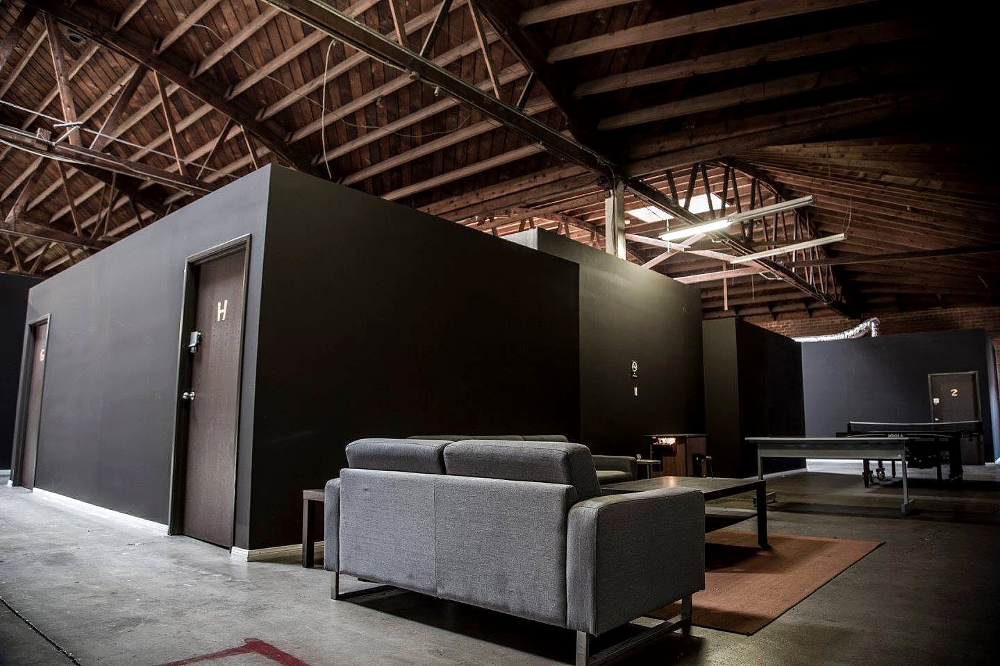 Players lounge with grey couches beside black studio walls under an exposed wooden truss ceiling