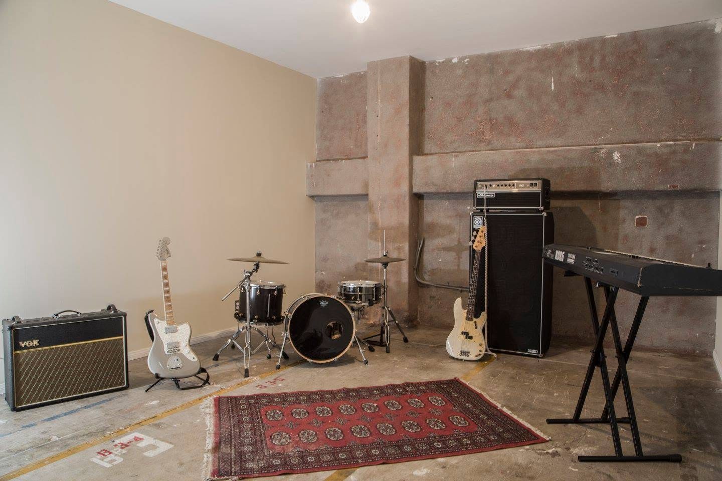 Studio with concrete accent wall, drum kit, guitar amps and keyboard